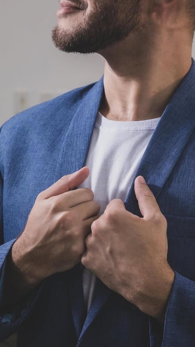 Homem usando terno azul, com barba, olhando para o horizonte.
