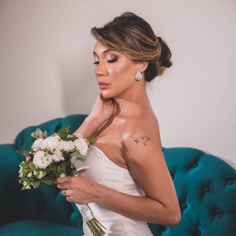 Noiva produzida em Governador Valadares, na suíte da noiva do Ateliê SF Beauty, Usando uma maquiagem preciosa, um penteado elegante com coque, vestido de noiva e segurando um buquet de flores brancas