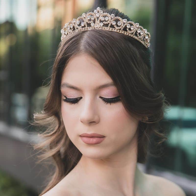 Dia de princesa em Governador Valadares, debutante com maquiagem delicada, penteado de cabelos ondulados e uma coroa na cabeça.