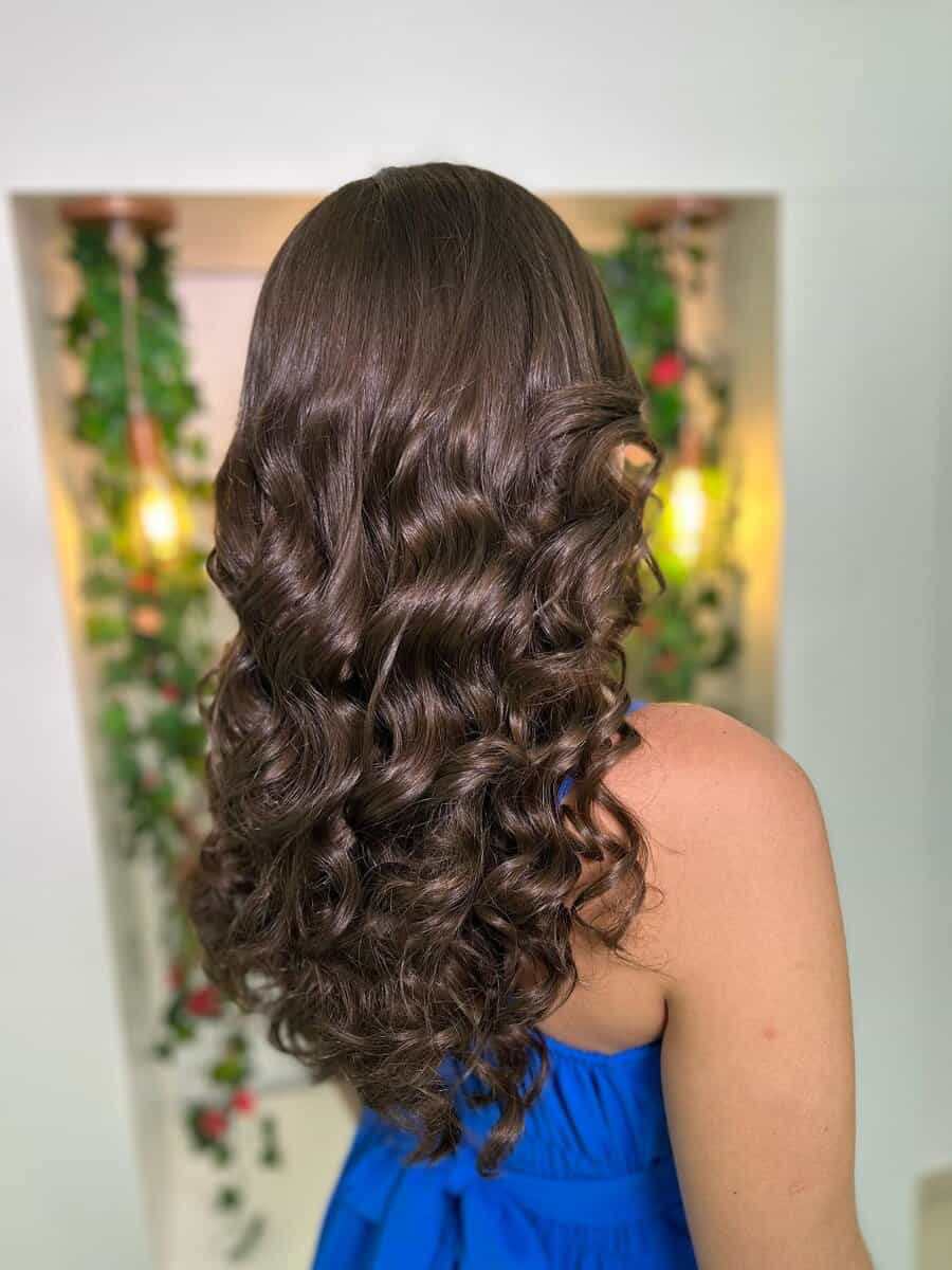 Resultado de uma escova modelada em cabelo castanho longo, mostrando cachos definidos e com brilho.
