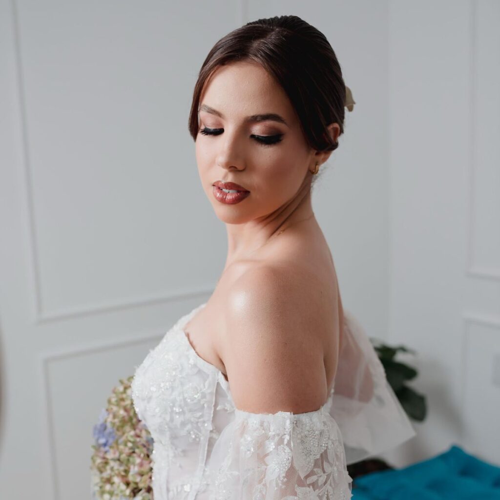 Noiva elegante com maquiagem beauty à prova d'água, resistente a lágrimas e durável. Penteado de cabelos lisos com coque bem elaborado. Vestido de noiva e buquê de hortênsias nas mãos