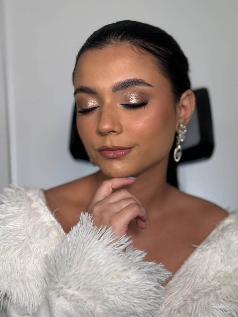Maquiagem sofisticada com glitter dourado e pele iluminada, realçando a beleza natural para eventos especiais.