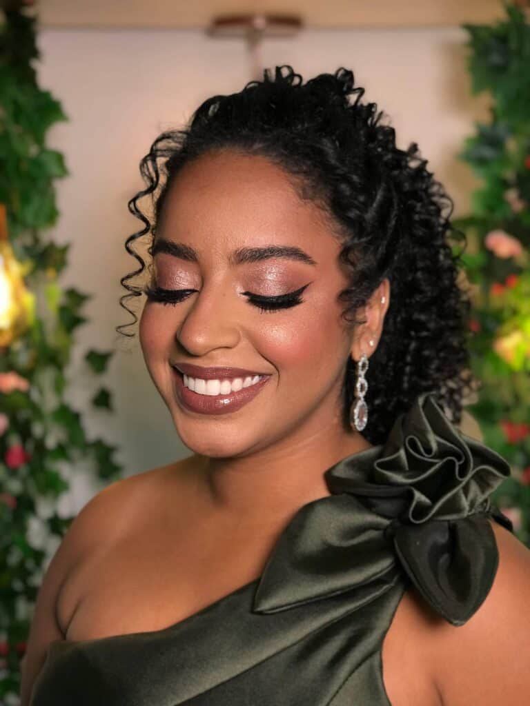 Imagem de mulher com maquiagem sofisticada e cabelo cacheado, usando vestido elegante com laço no ombro, ideal para beleza e eventos, destacando o trabalho do Ateliê SF Beauty.